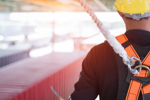 Mitarbeiter trägt Helm und ist mit Seil gesichert. Die Themen Sicherheit und Gesundheit am Arbeitsplatz sind für Arbeitgeber und -nehmer essentiell. © Shutterstock, Aunging
