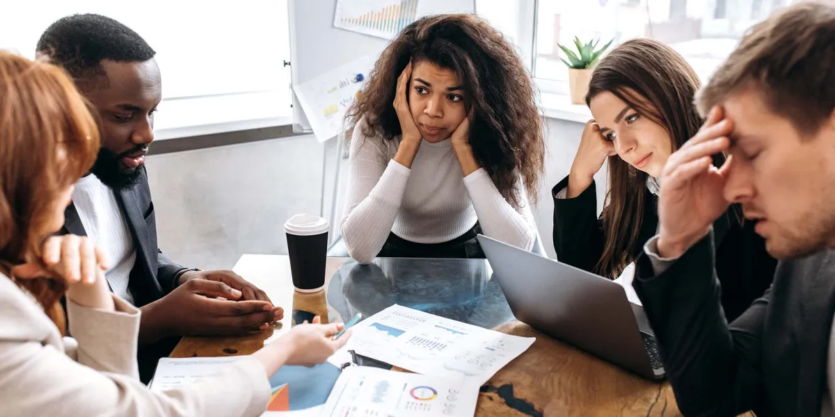 Mitarbeiter sitzen um Tisch und sind besorgt angesichts der Geschäftsrisiken, die 2025 drohen. © Adobe Stock, Kateryna