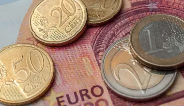 Mehrere Euro Münzen liegen auf einem Zehn Euro Geldschein als Symbol für den Anstieg des Mindestlohns.