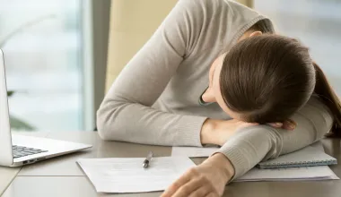 Eine erschöpfte Mitarbeiterin, die ein hohes Arbeitspensum bewältigen muss, leidet unter psychischen Belastungsfaktoren. © Shutterstock, fizkes