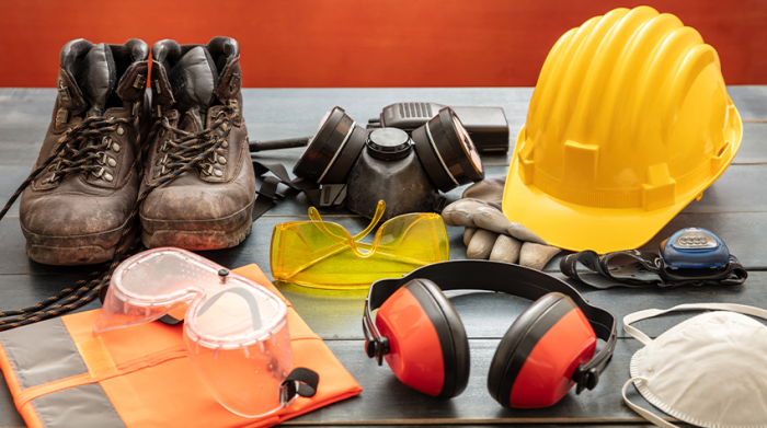 Persönliche Schutzausrüstung, wie Sicherheitsschuhe, Ohrenschutz, Kopfschutz oder Mundschutz liegen auf einer Arbeitsfläche bereit. © Adobe Stock, Rawf8 