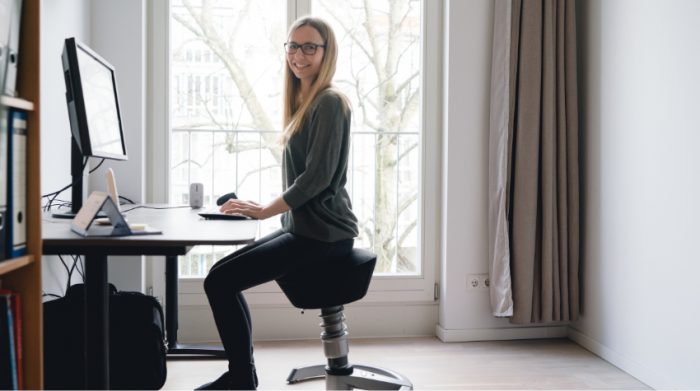 Frau sitzt am Schreibtisch auf einem Hocker. © Adobe Stock, Kevin Sloniecki