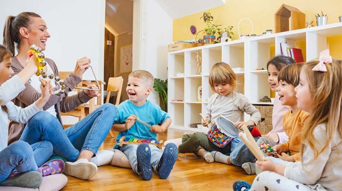 Kindergärtnerin musiziert mit Kindern in einem Betriebskindergarten. © Adobe Stock, lordn