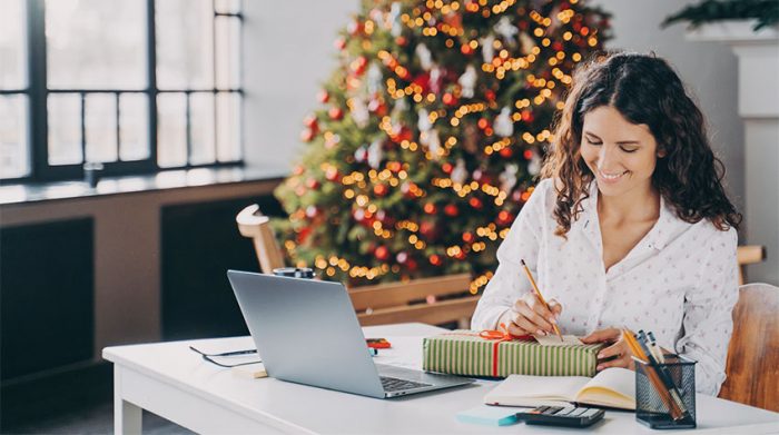 Frau sitzt an einem Arbeitsplatz im Büro und beschriftet ein Geschenk. © Adobe Stock, VK Studio