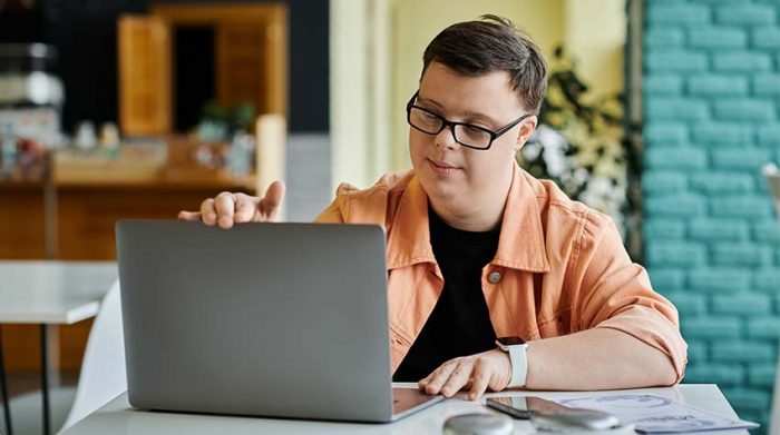 Junger Mann mit Down Syndrom benutzt barrierefreies Notebook und Smartphone. © Adobe Stock, Bliss