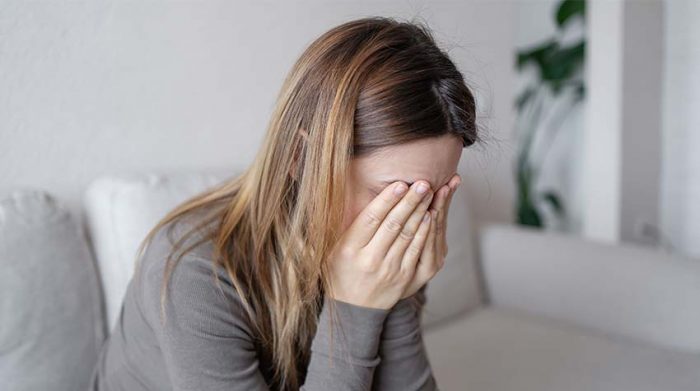 Frau sitzt mit Depression auf dem Sofa. Die erlebte Gewalt am Arbeitsplatz belastet sie. © Adobe Stock, Julija